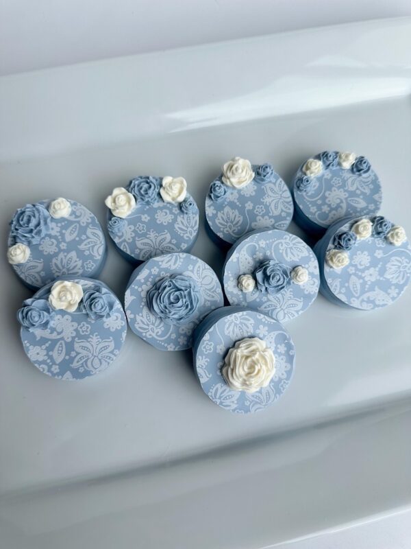 Eight Dusty Blue White Paisley chocolate-covered Oreos with white floral designs and rose embellishments, displayed on a white surface.