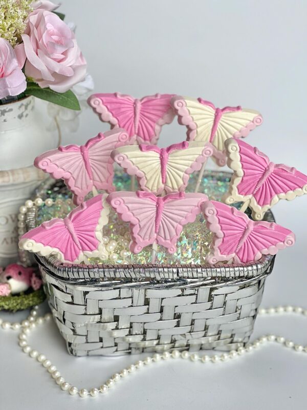 A white wicker basket contains 12 "Pretty in Pink" butterfly-shaped cookies, surrounded by decorative pearls and a vase of roses.