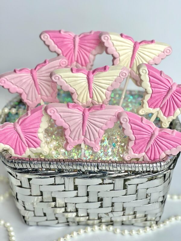 A silver woven basket holds 12-Pretty in Pink Butterfly Lollipops, butterfly-shaped cookies on sticks with intricate icing details, set against a neutral background. Perfect for birthday parties, showers, gifts, garden parties, or baby girl celebrations.