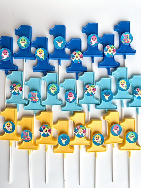 Baby Shark-themed, #1-shaped chocolate lollipops for a first birthday are organized in blue, yellow, and light blue on a white background.
