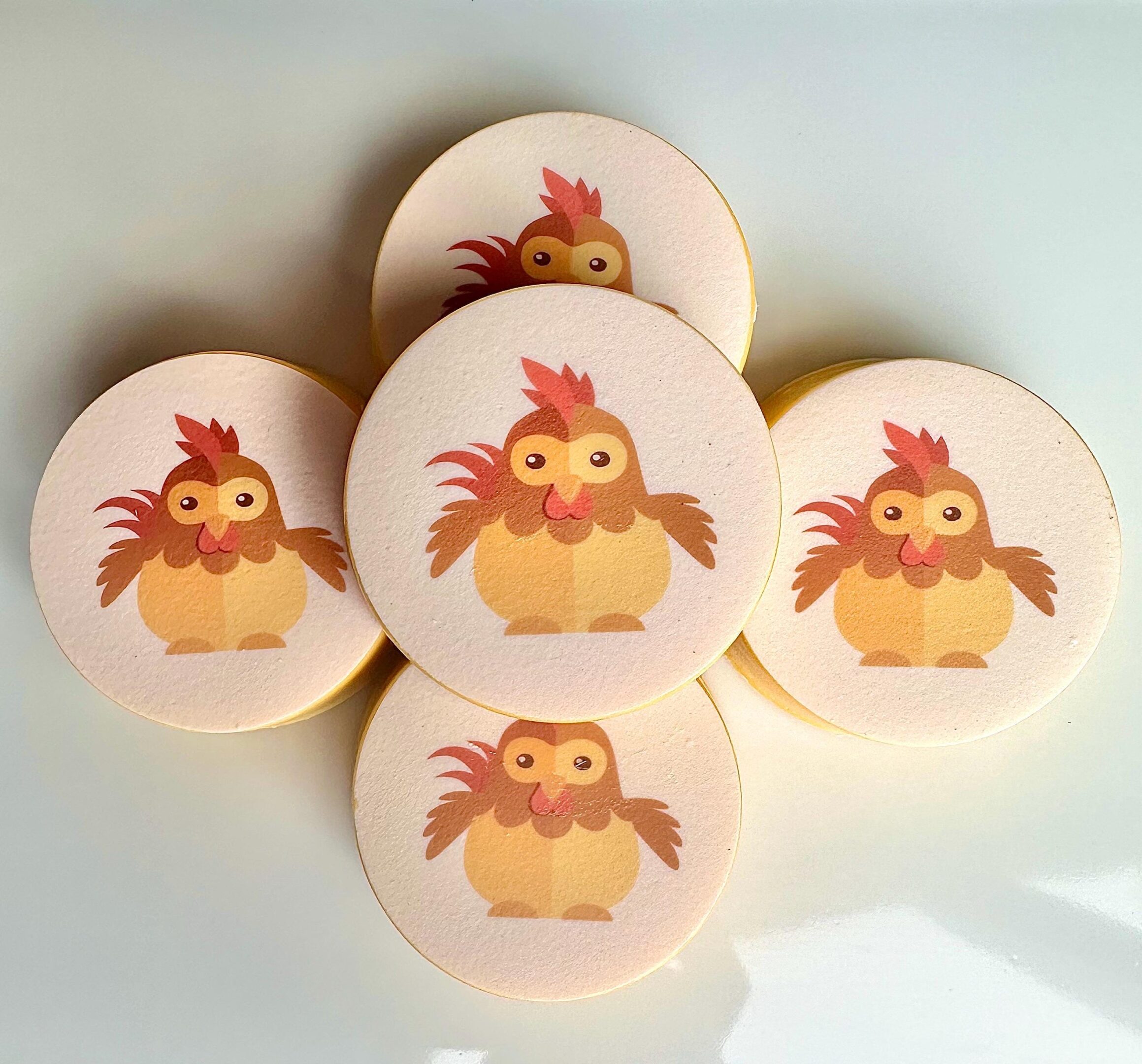 Five chocolate-covered Oreo favors, each designed with a baby chicken cartoon, are arranged in a circle on a white background.