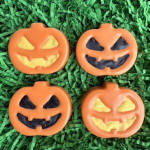 Four pumpkin decorations on green shredded paper.