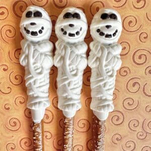 Three mummy-shaped chocolate-covered pretzel sticks.