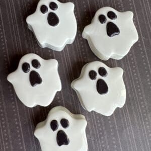 Five ghost-shaped Halloween cookies on table.