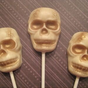 Three skull-shaped lollipops on patterned background.